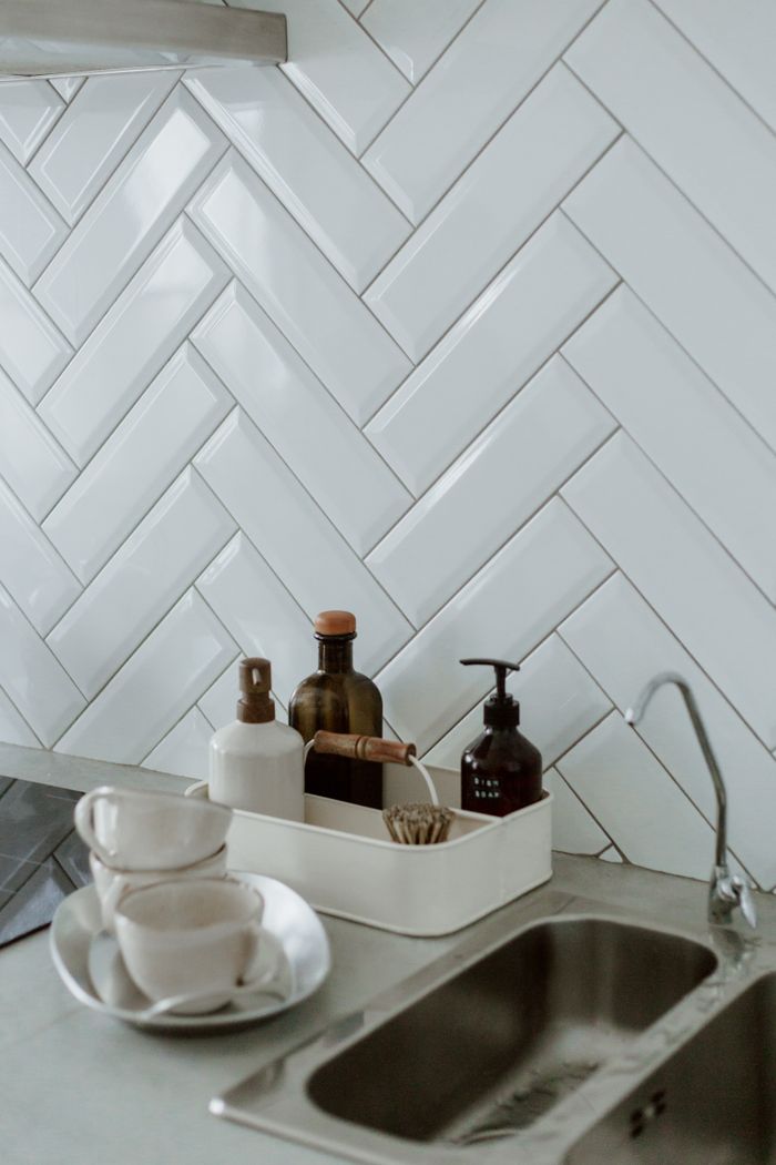 why-choose-us Stylish kitchen sink area with cleaning products and cups on a tiled counter.