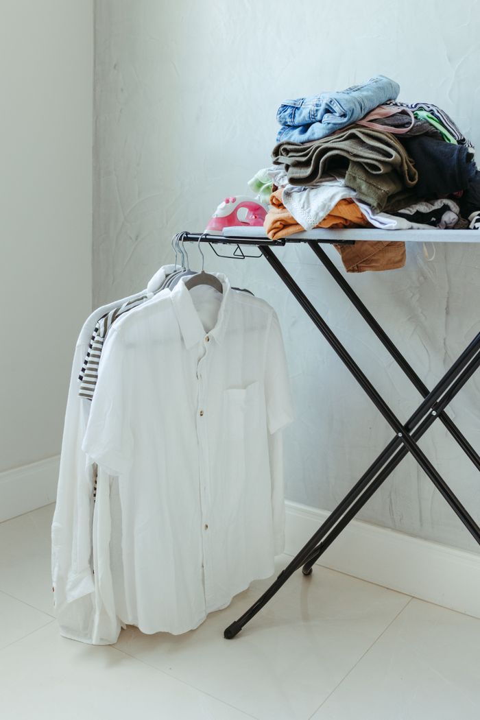 portfolio-03 Neatly folded clothes on ironing board with hanging shirts in a tidy laundry setup.