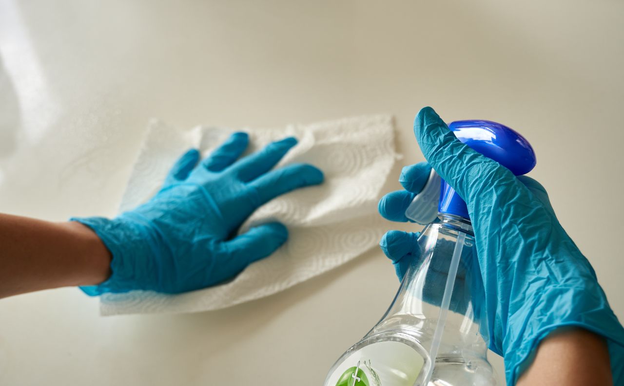 portfolio-02 Close-up of gloved hands using disinfectant spray and cloth for cleaning surface.