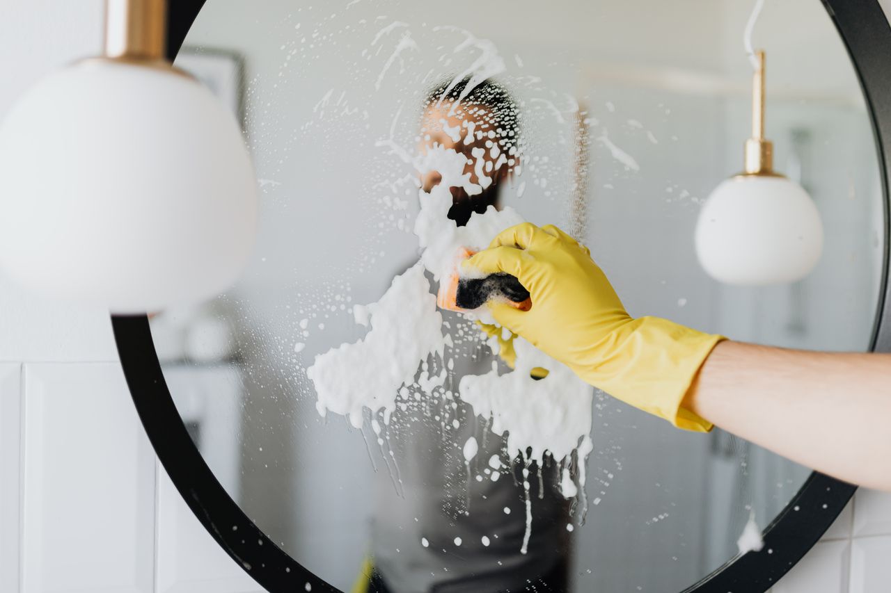 portfolio-06 Anonymous male housekeeper in yellow rubber gloves wiping foam from round mirror in bathroom