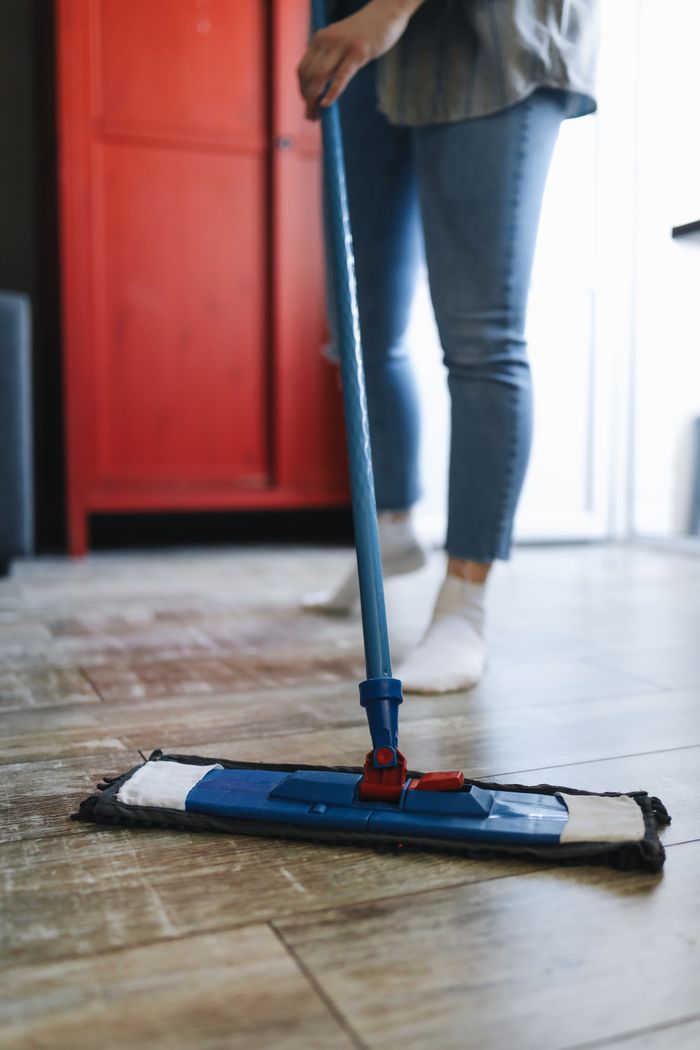 stats-img A woman mops a wooden floor in a modern living room with a red cabinet, emphasizing cleanliness.